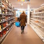 reduce food waste ukds blog woman walking down the middle of a supermarket aisle carrying a blue basket. Shelves are full, we cannot see her face