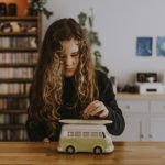 how to talk to kids about money ukds blog young girl with curly hair putting money into her vw camper piggy bank